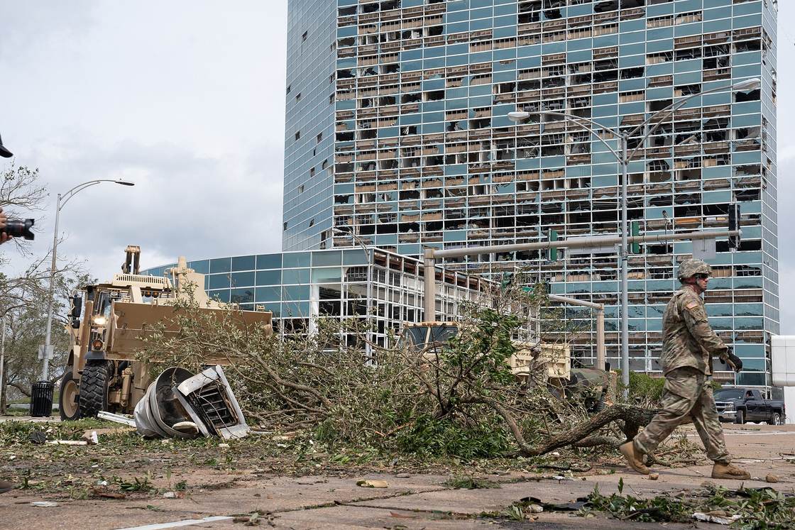 A downtown Lake Charles high-rise with most of its windows blown out, debris and fallen trees in the street below